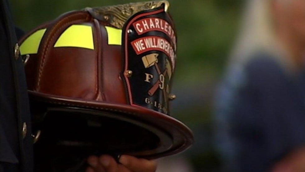 A firefighter holds a helmet in tribute to the Charleston 9 at a memorial service. (Source:...